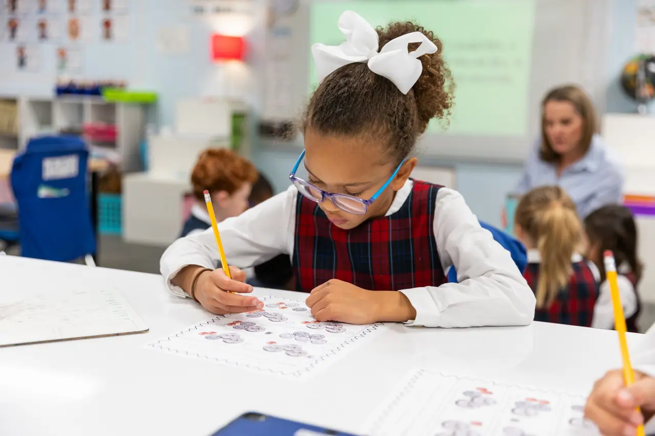 Lower School student works on a coin-counting worksheet while her teacher leads the class