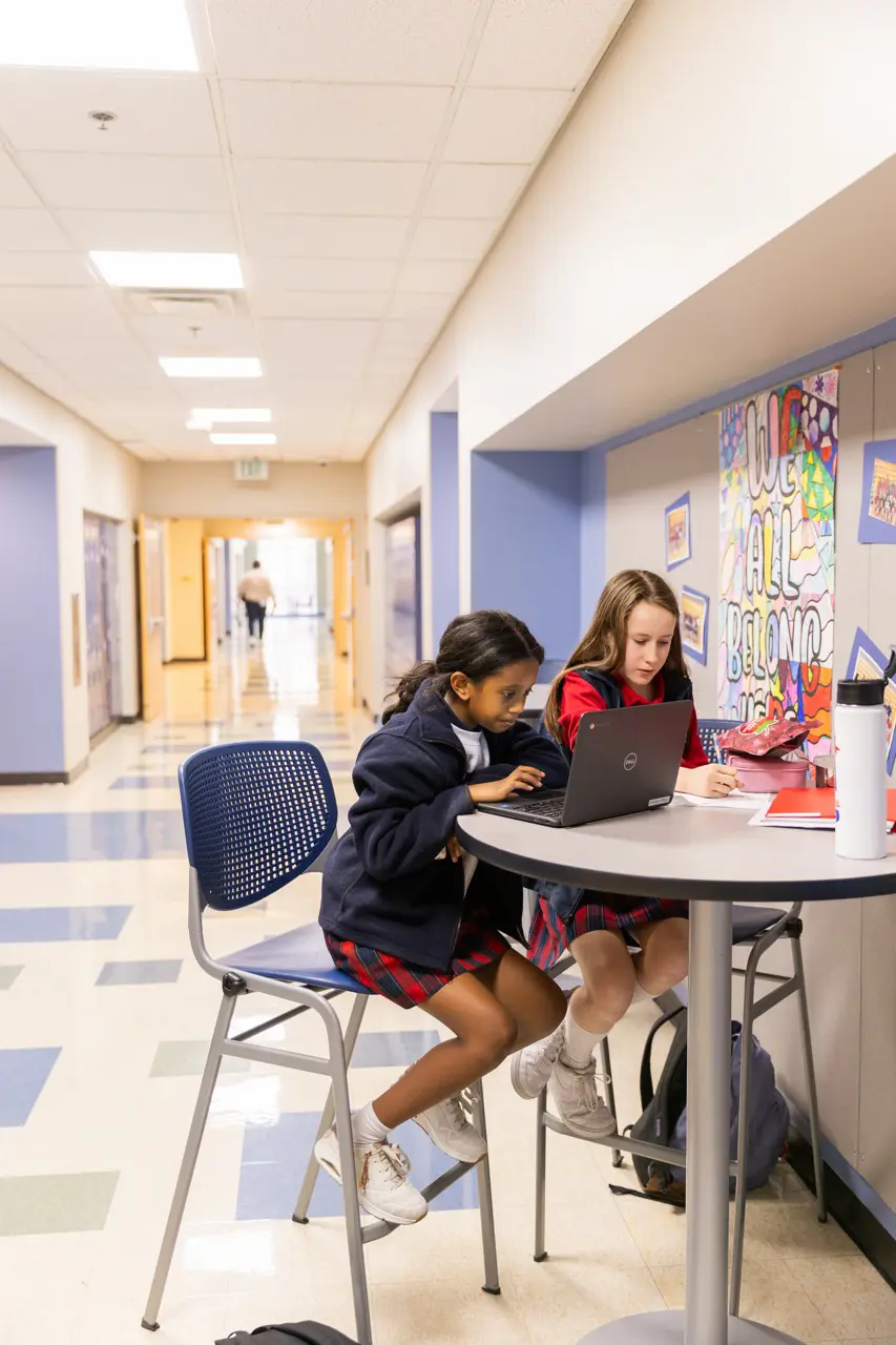 Two students working on a laptop in a school hallway