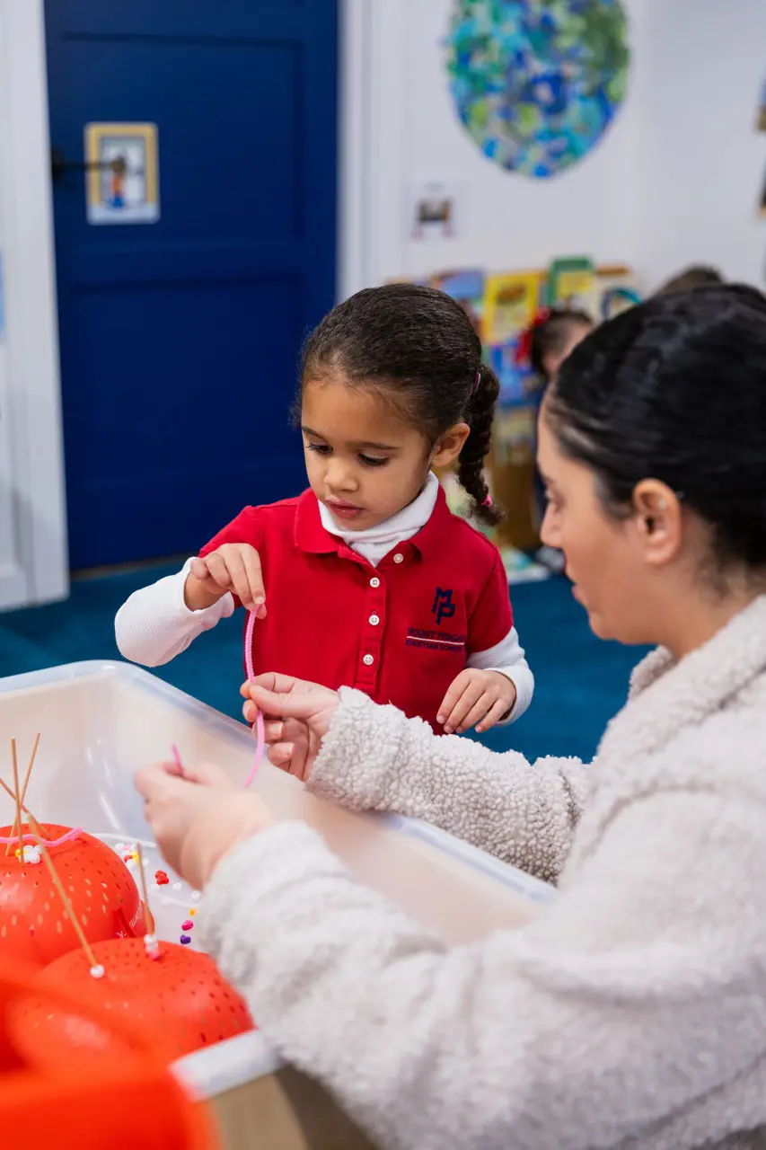 Preschooler threading beads with her teacher