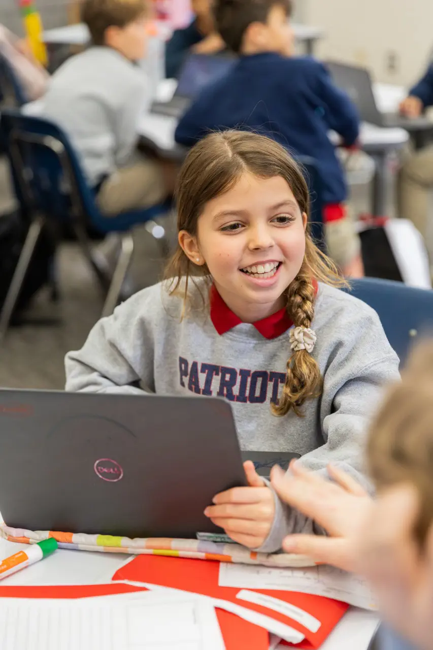 Student smiling while working on a laptop with classmates