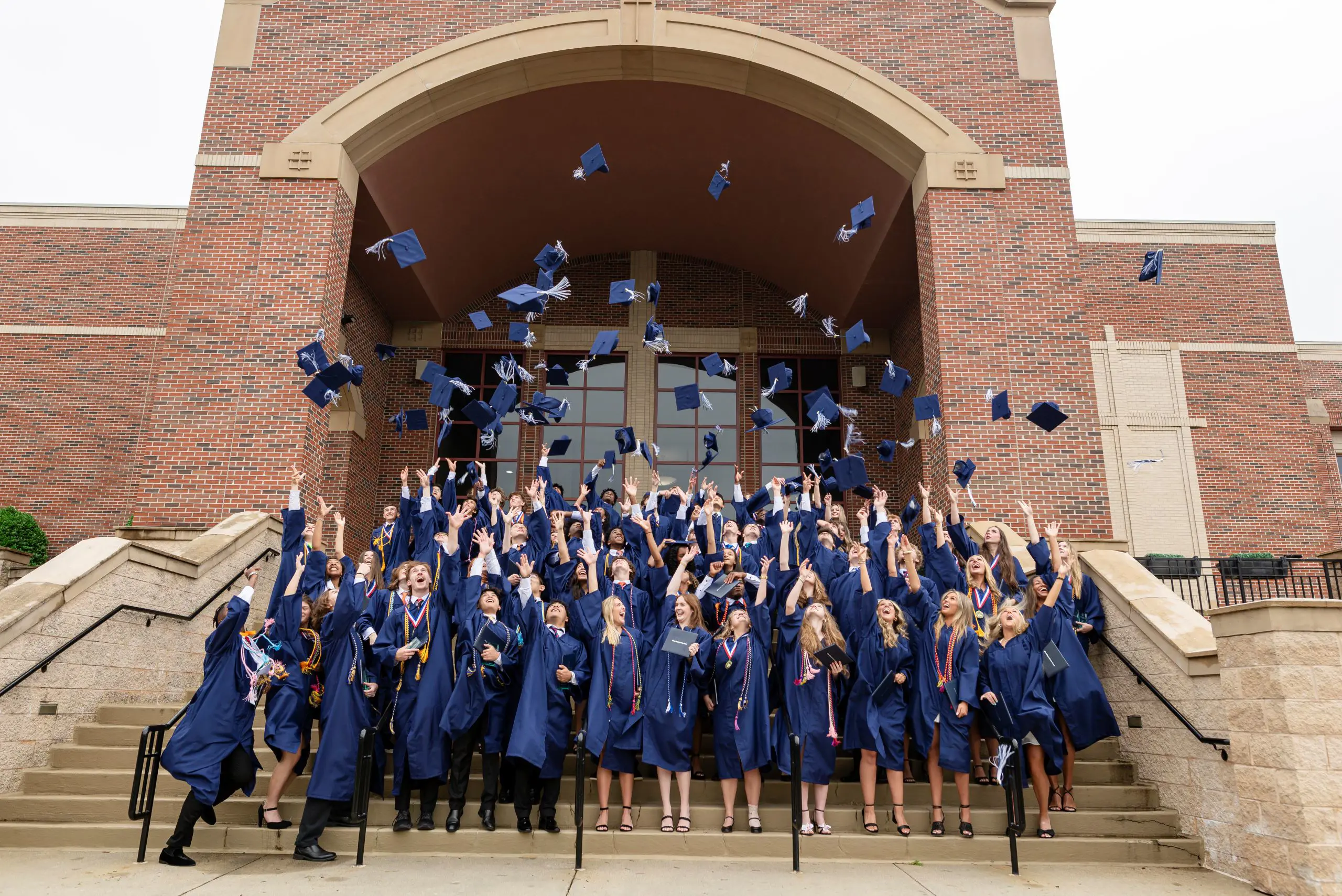 Students tossing graduation gaps in the air, standing on steps