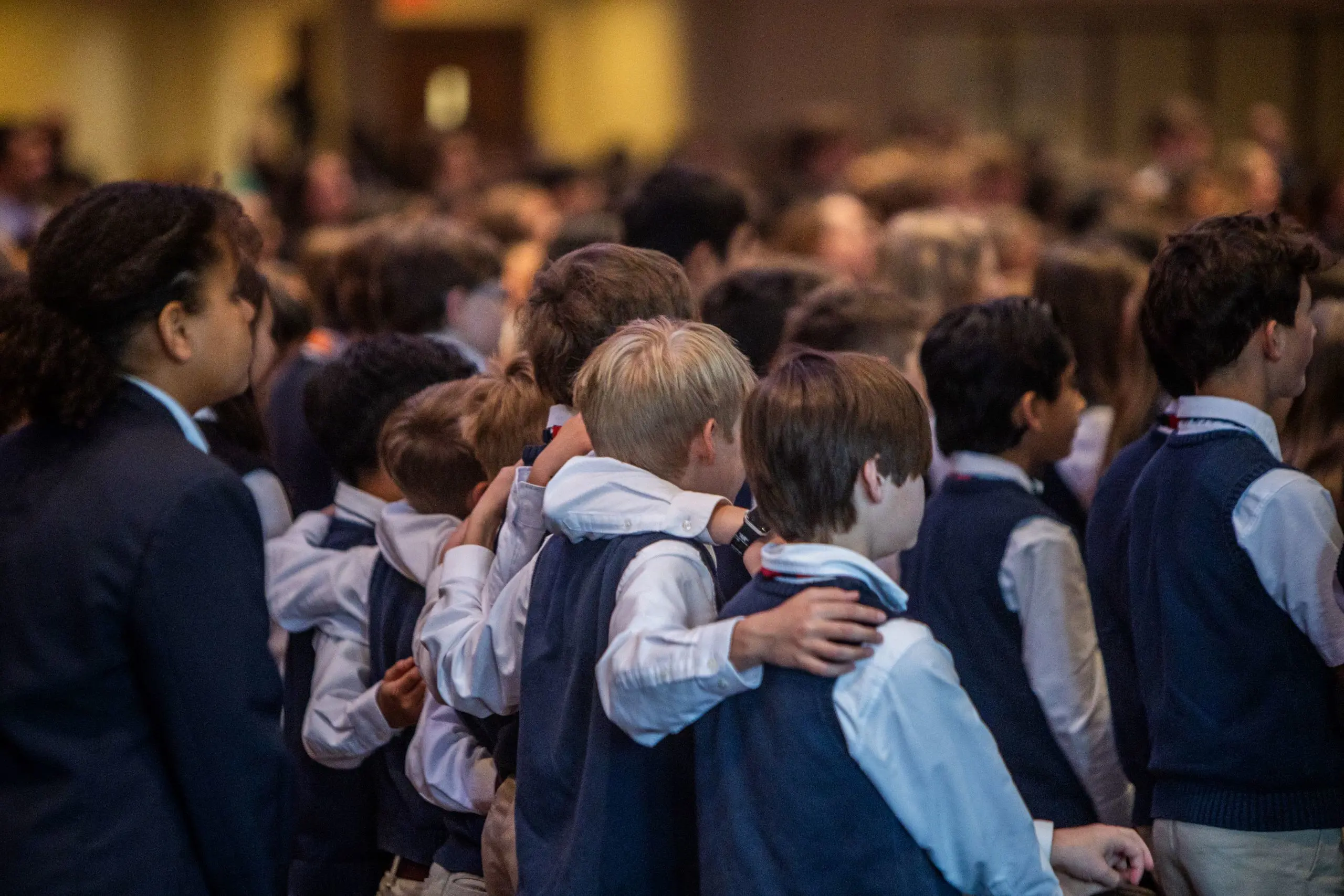 Group of students singing with arms around each other, from behind