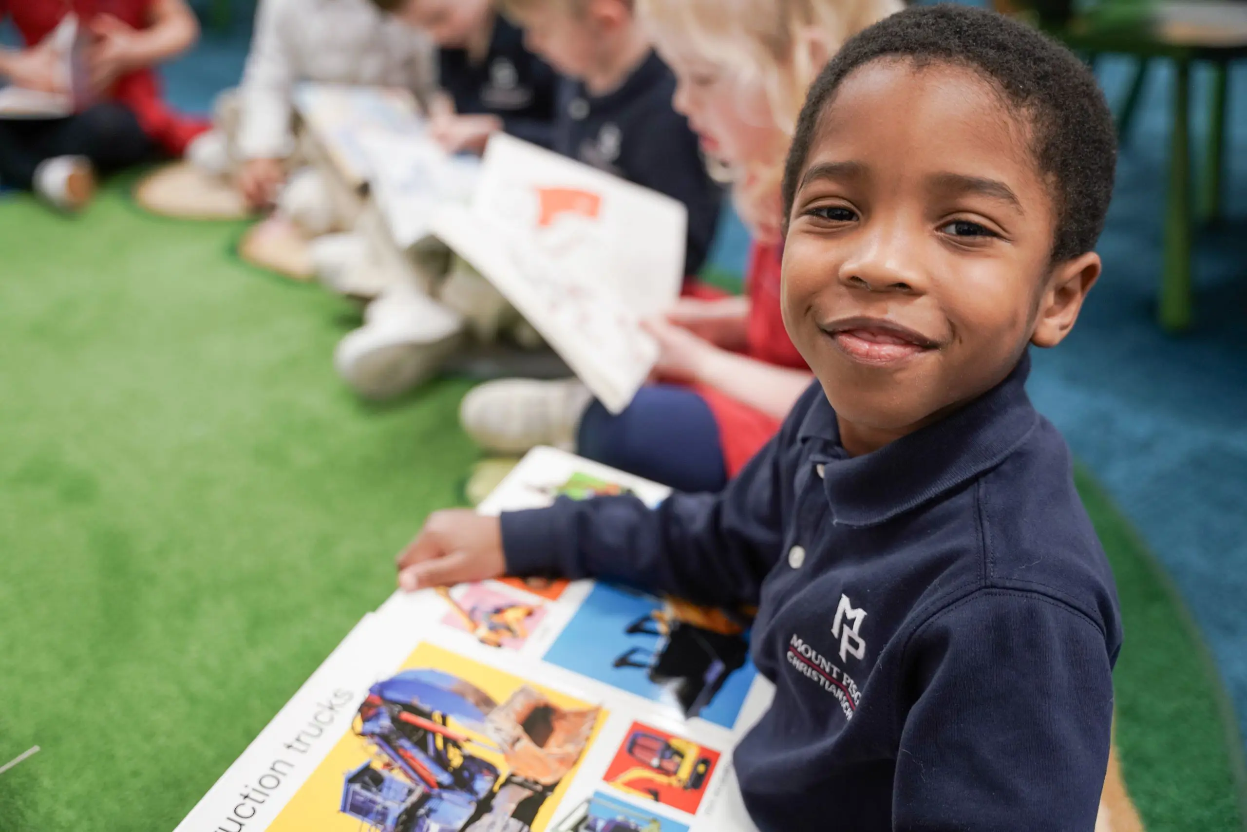 Young boy smiles at the camera, looking up from his book