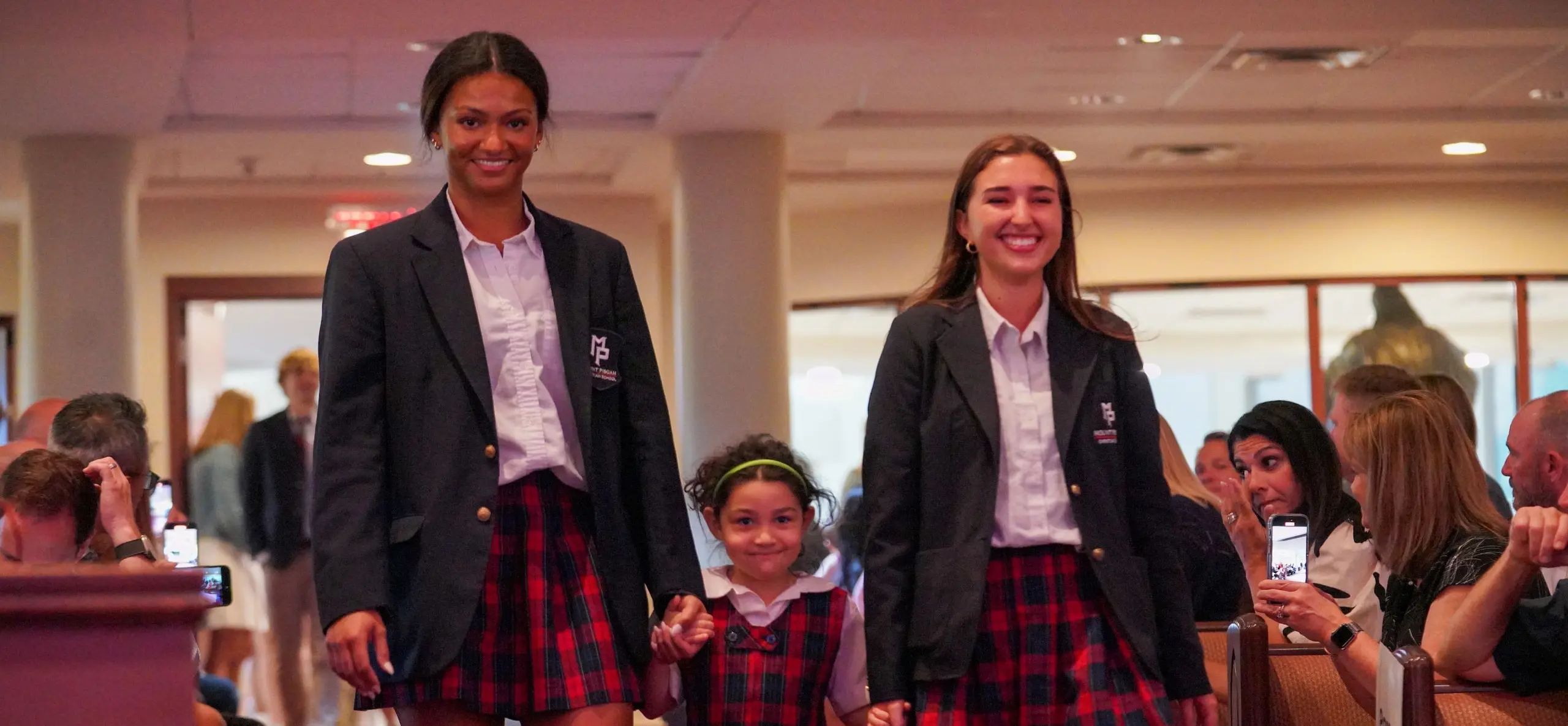 Two students holding hands of a younger student, leading her 