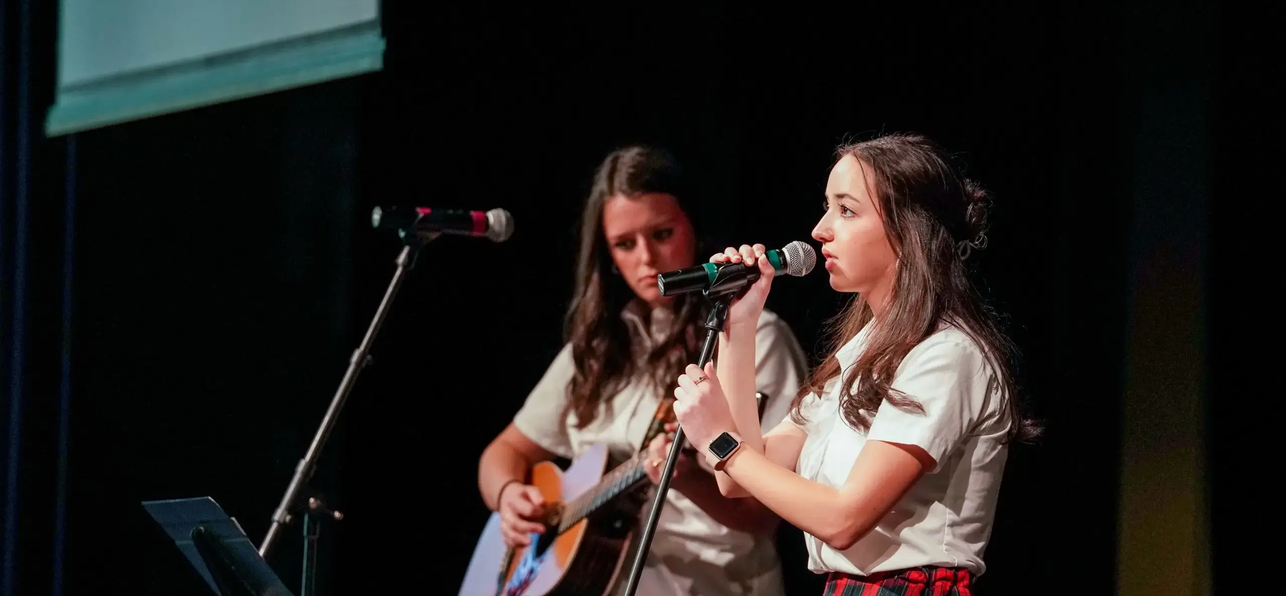 Two students performing onstage, one singing and the other playing guitar