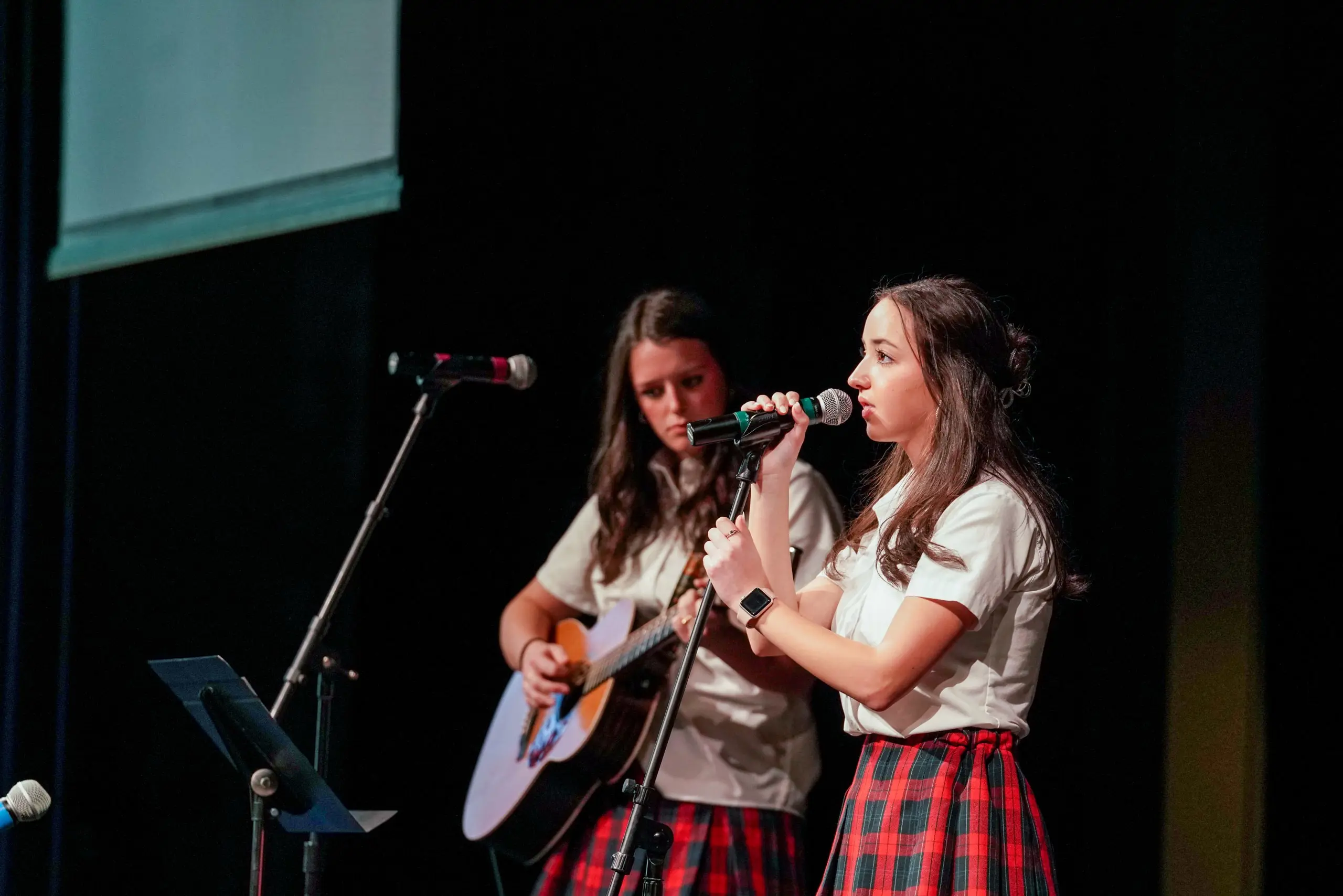 Students performing onstage, one singing and the other playing guitar